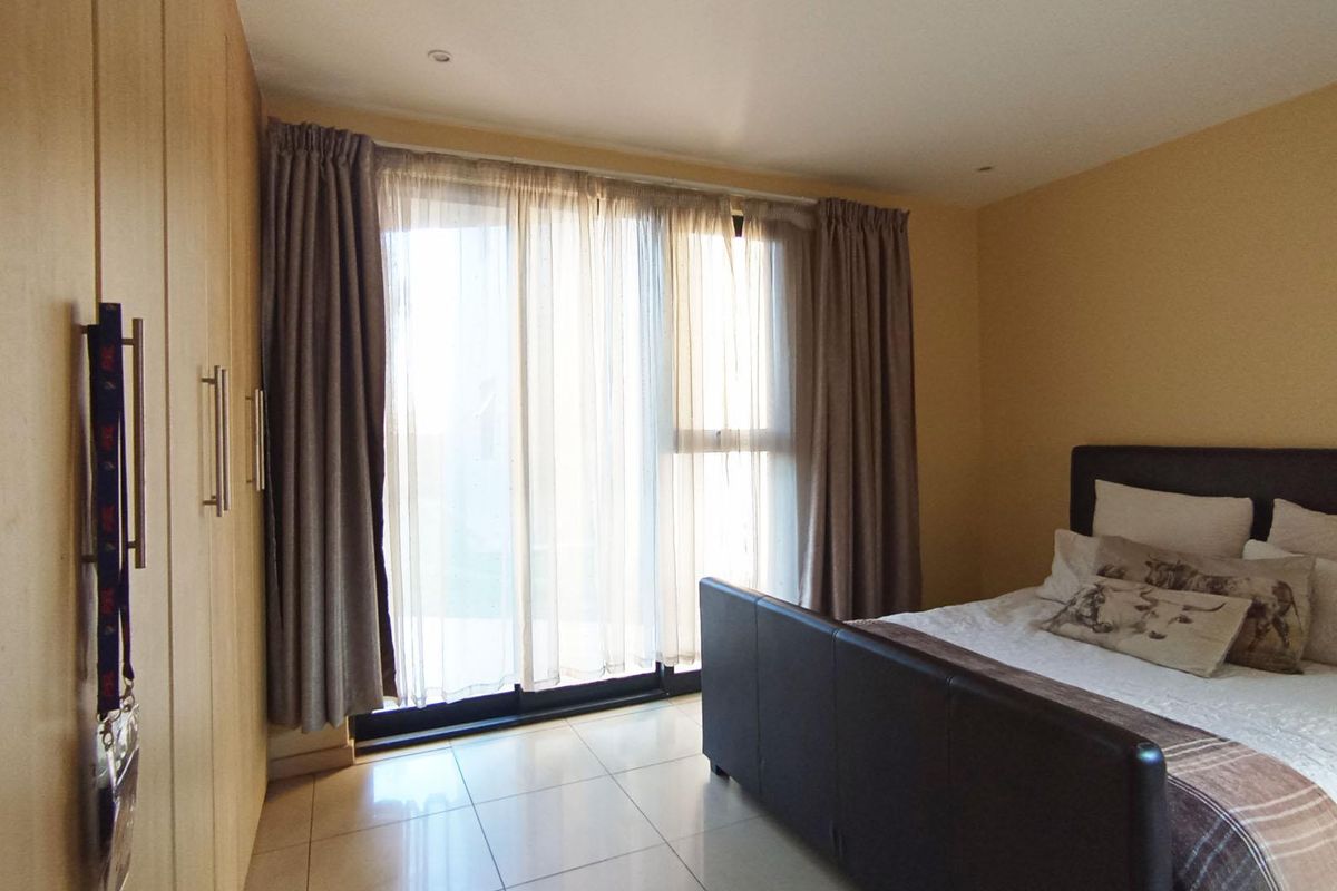 A well-lit bedroom featuring built-in wooden wardrobes, tiled flooring, and sliding glass doors that provide access to an outdoor area.
