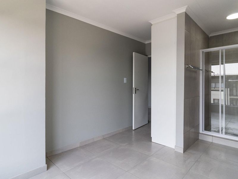 A clean, modern bathroom featuring a pedestal basin, a glass-enclosed shower, and neutral floor-to-ceiling tiling.