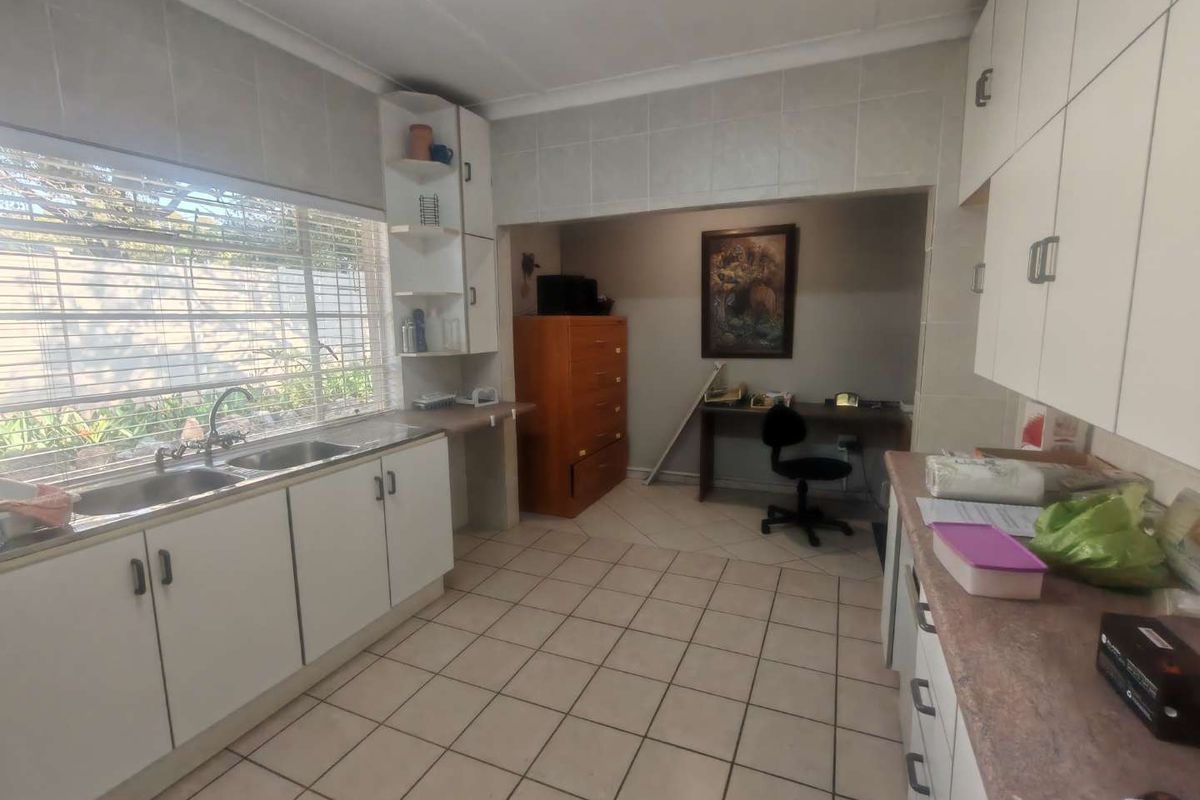 Functional kitchen featuring tiled flooring, ample built-in cabinetry, double basin sink, and a large window providing natural light, with an adjacent workspace area.
