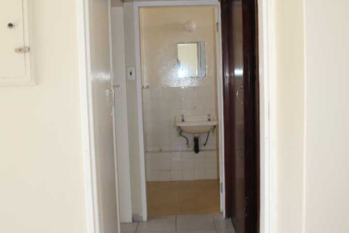 A functional hallway leading to a bathroom, featuring tiled flooring and built-in storage cupboards.