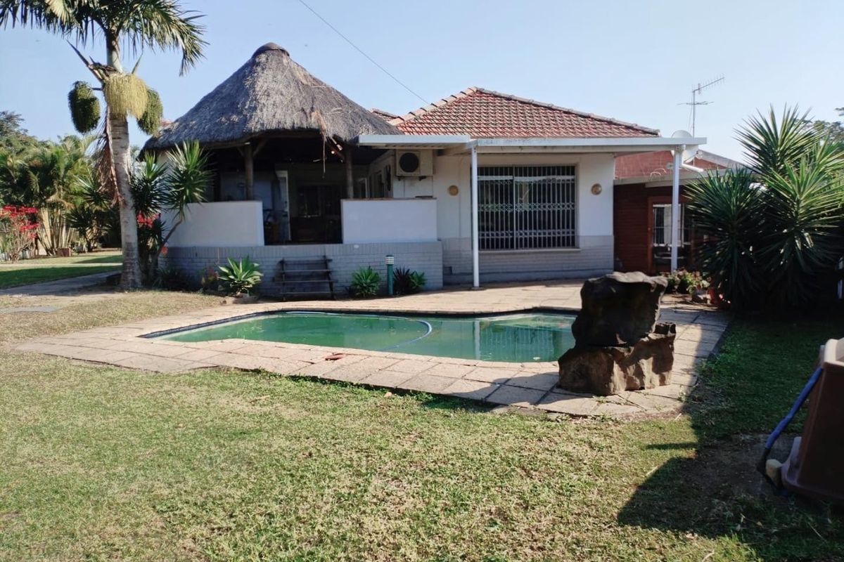 Rear exterior view featuring a swimming pool, paved patio, and a traditional thatched lapa structure attached to the main house.