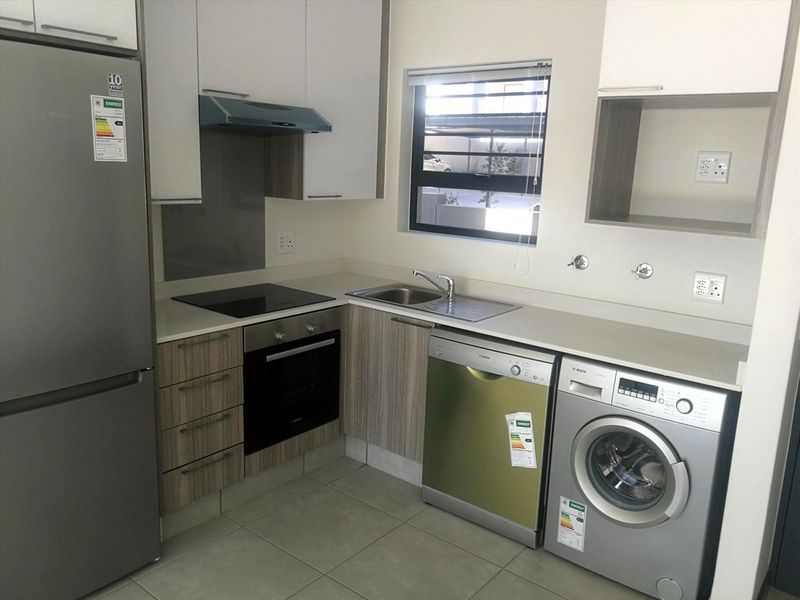 Modern kitchen featuring built-in cabinetry, electric hob, oven, extractor fan, and integrated plumbing connections for laundry and dishwasher appliances.