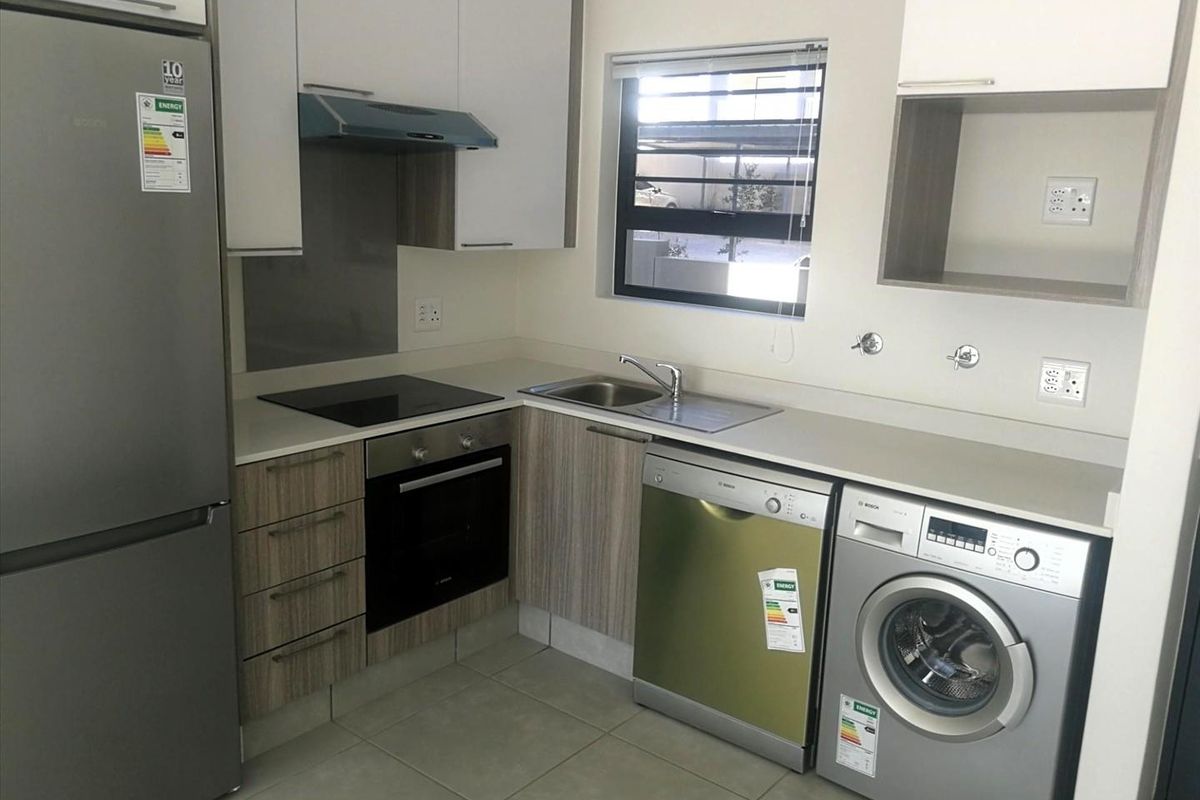Modern kitchen featuring built-in cabinetry, electric hob, oven, extractor fan, and integrated plumbing connections for laundry and dishwasher appliances.