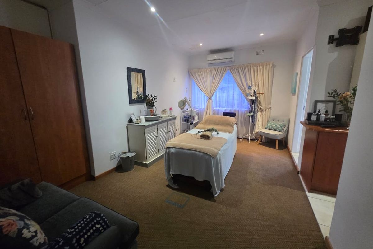 A functional bedroom space currently utilized as a treatment room, featuring built-in cabinetry, wall-mounted air conditioning, and carpeted flooring.