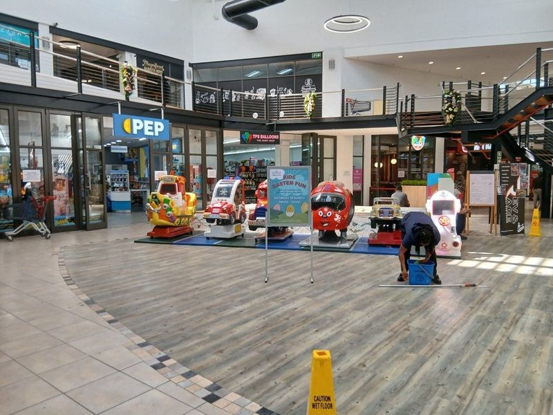 Interior view of a retail shopping centre atrium featuring a mezzanine level, glass storefronts, and a combination of wood-look and tiled flooring.