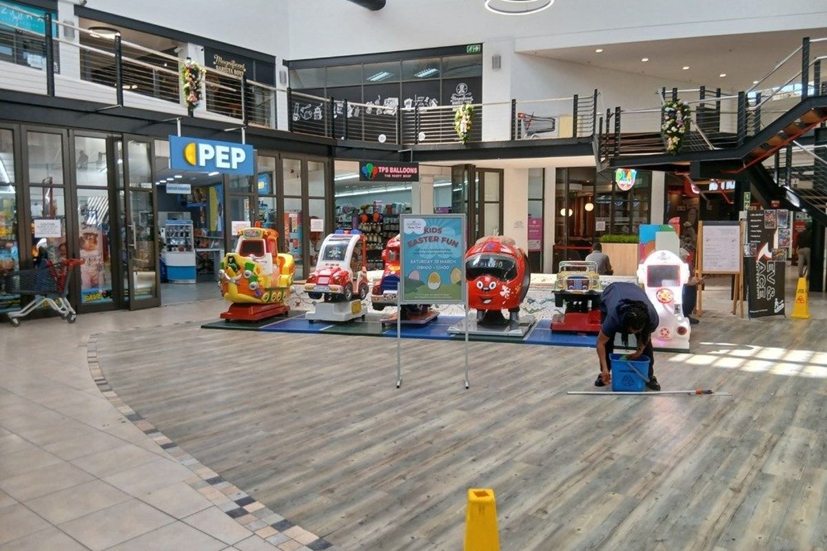 Interior view of a retail shopping centre atrium featuring a mezzanine level, glass storefronts, and a combination of wood-look and tiled flooring.