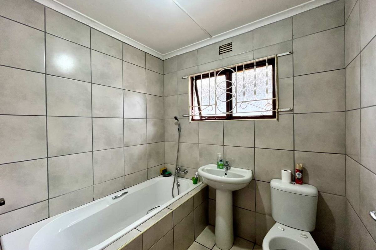 A functional bathroom featuring a bathtub, pedestal basin, and toilet, finished with neutral wall and floor tiles.