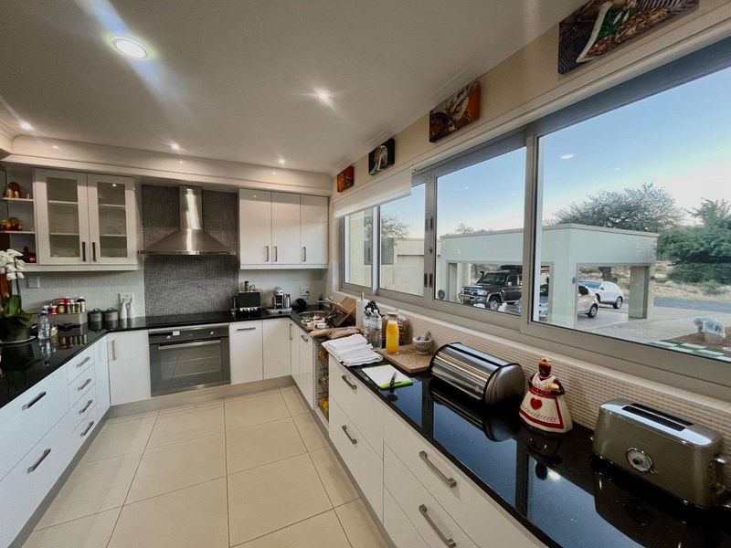 Modern kitchen featuring white cabinetry, black granite countertops, stainless steel appliances, and large windows providing ample natural light.