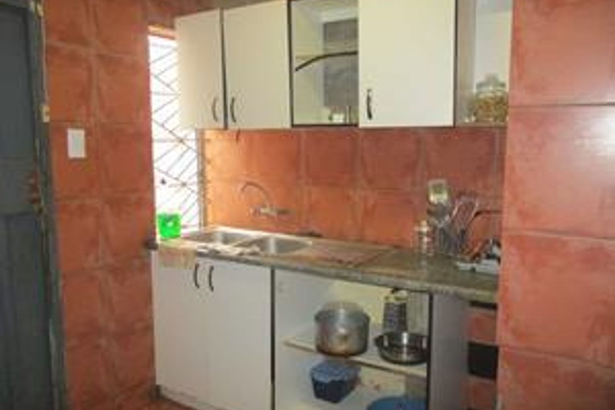 A compact kitchen area featuring built-in cabinetry, a double sink, and full-height wall tiling.