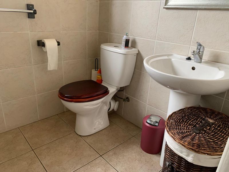 A functional bathroom featuring a pedestal basin, standard toilet, and neutral wall and floor tiling.