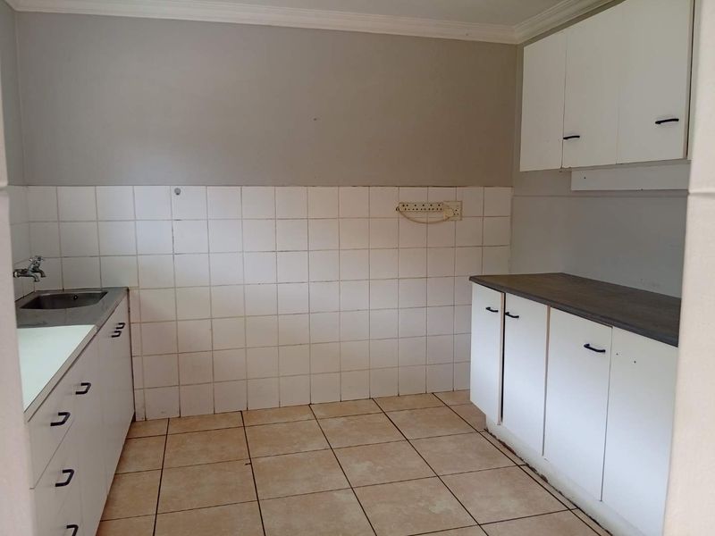 A functional, empty kitchen featuring white built-in cabinetry, laminate countertops, a stainless steel sink, and tiled flooring, ready for a modern update.