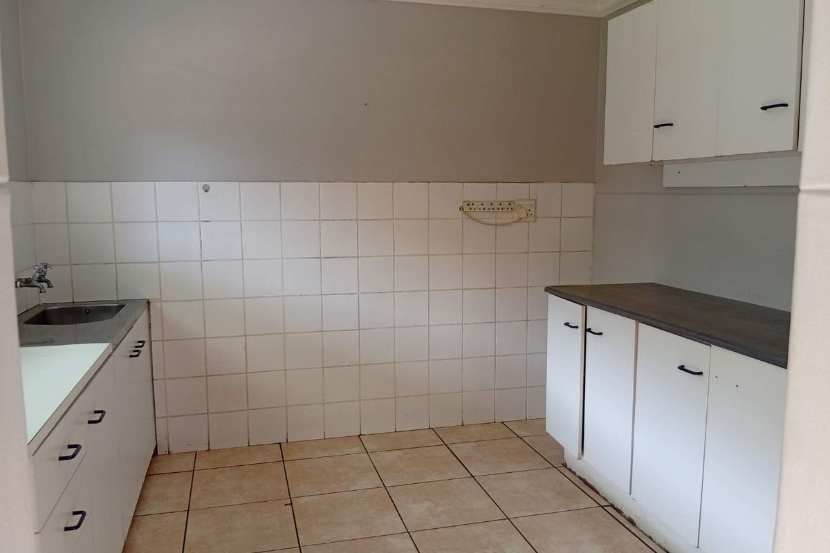 A functional, empty kitchen featuring white built-in cabinetry, laminate countertops, a stainless steel sink, and tiled flooring, ready for a modern update.