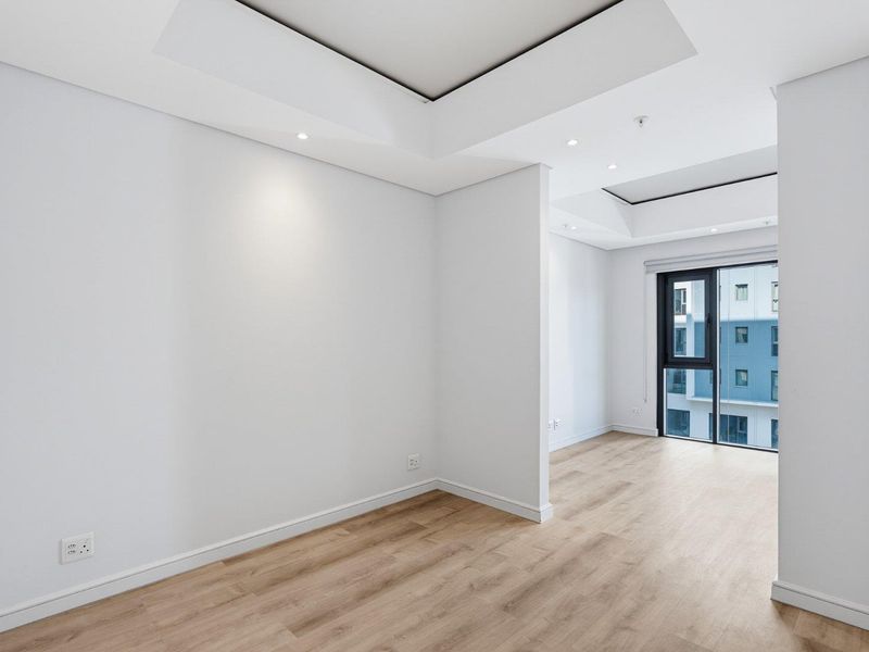 A bright, modern, and empty living area featuring recessed ceiling details, laminate flooring, and a large sliding glass door providing natural light.