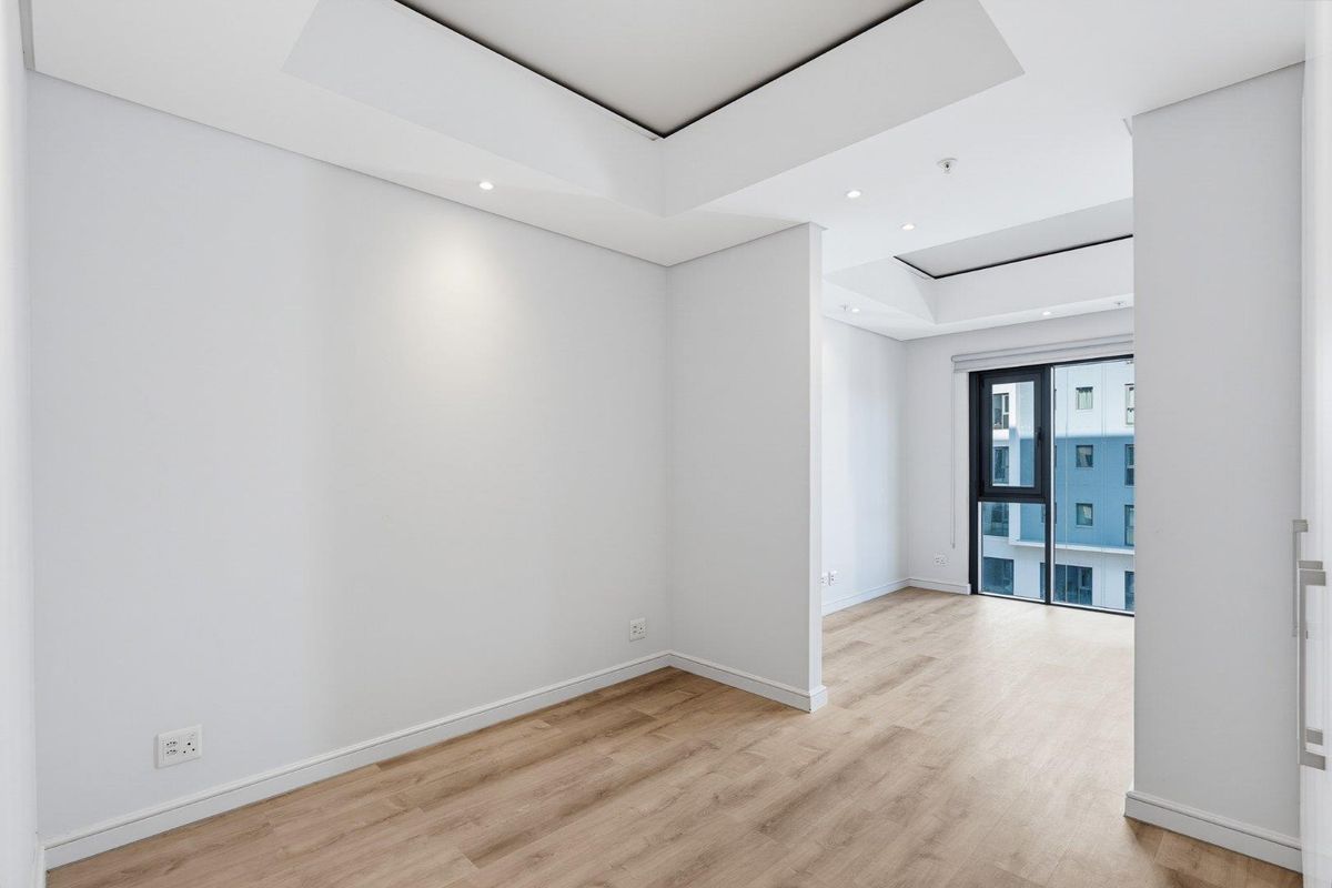 A bright, modern, and empty living area featuring recessed ceiling details, laminate flooring, and a large sliding glass door providing natural light.