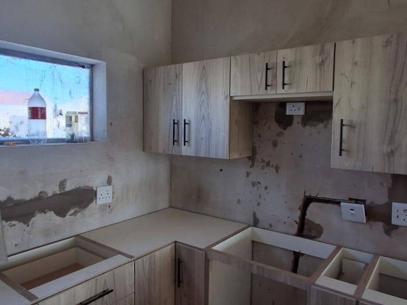 An unfinished kitchen space featuring installed laminate cabinetry, requiring wall finishing, backsplash installation, and final plumbing and electrical connections to complete the room.
