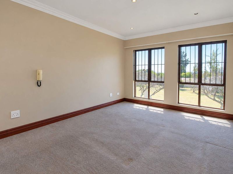 A spacious, empty bedroom featuring neutral walls, carpeted flooring, security bars on the windows, and an integrated intercom system.