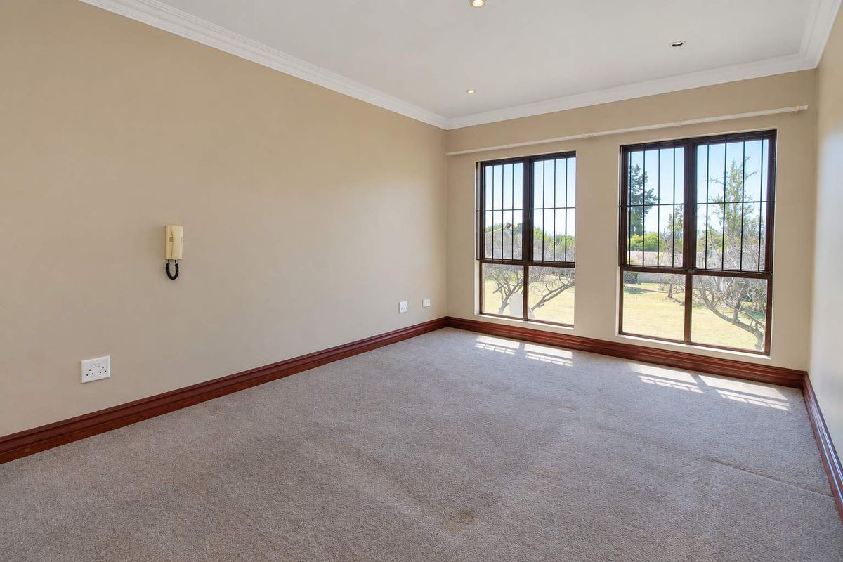 A spacious, empty bedroom featuring neutral walls, carpeted flooring, security bars on the windows, and an integrated intercom system.