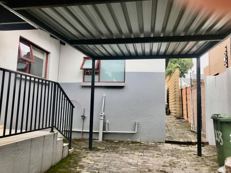 Rear exterior area featuring a corrugated metal carport, brick paving, and concrete stairs leading to the property entrance.
