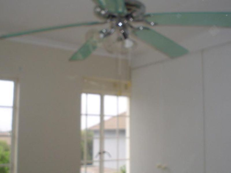 A bedroom featuring built-in cupboards, a ceiling fan, and large windows providing natural light.