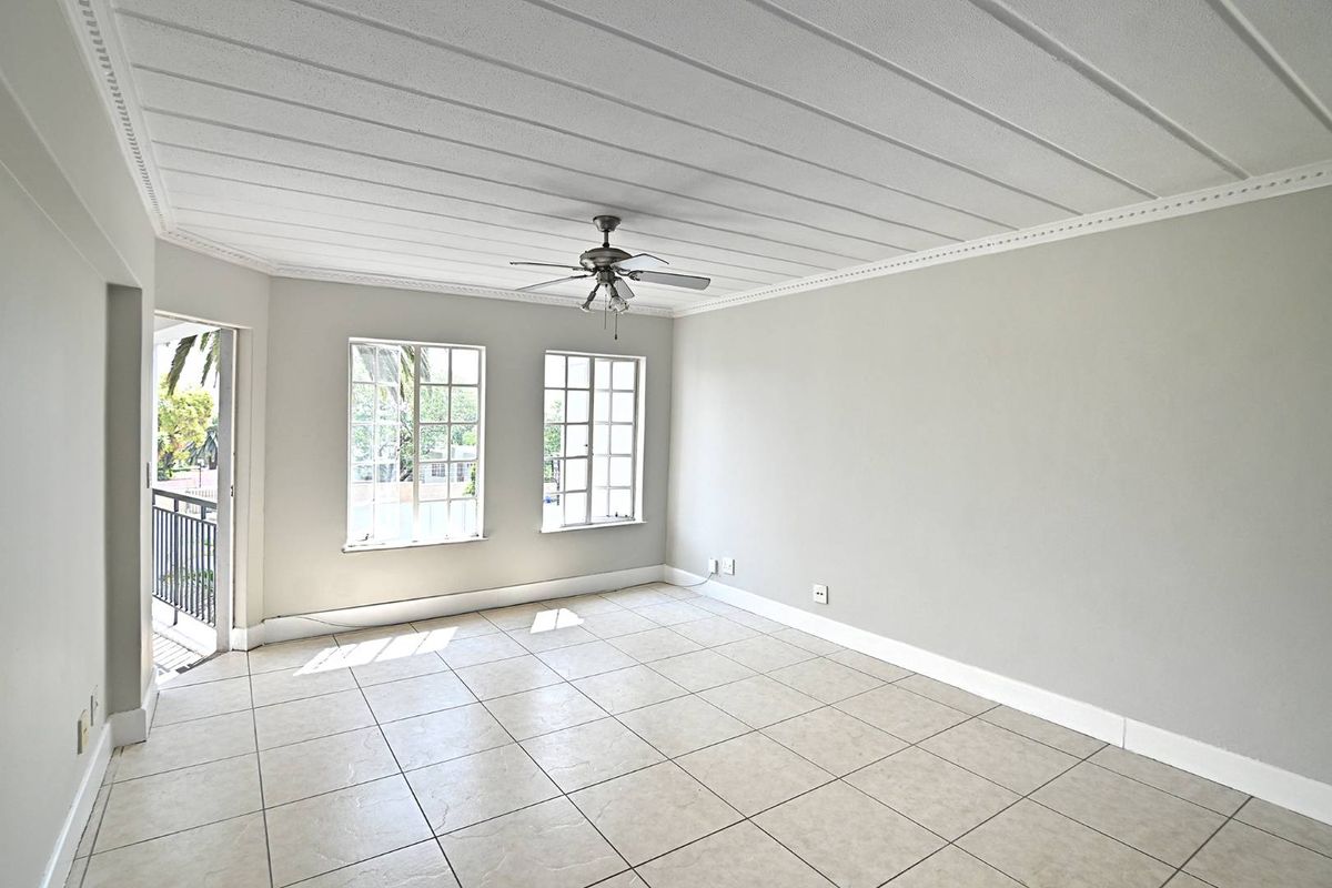 A bright, empty living room featuring tiled flooring, a ceiling fan, and access to a small balcony through a glass door.