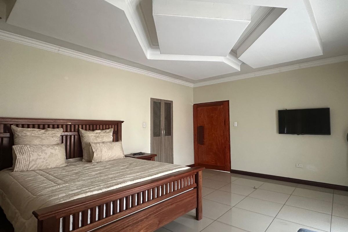 Spacious bedroom featuring tiled flooring, a decorative tray ceiling with recessed lighting, and a built-in wooden cupboard.