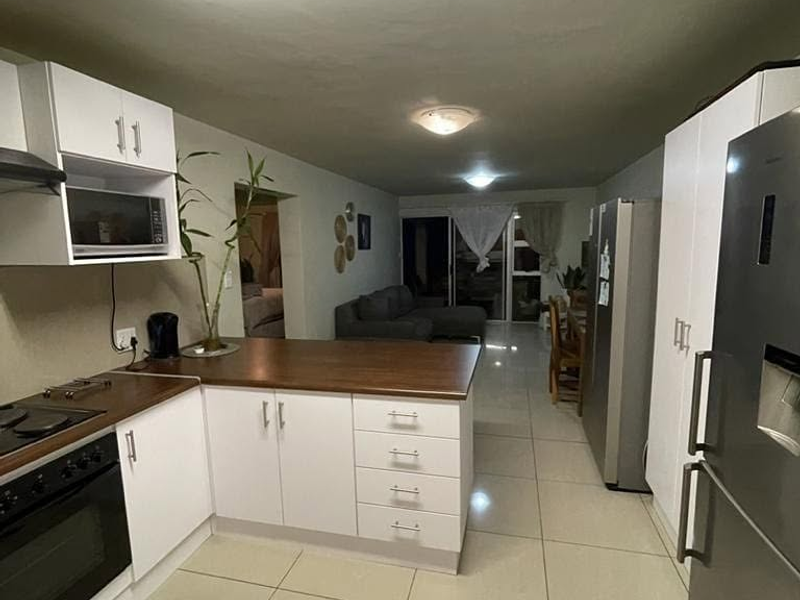 Open-plan kitchen and living area featuring white cabinetry, wooden countertops, built-in appliances, and neutral tiled flooring throughout the space.