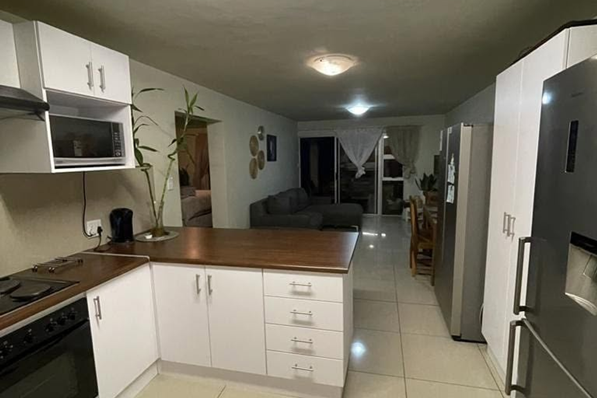Open-plan kitchen and living area featuring white cabinetry, wooden countertops, built-in appliances, and neutral tiled flooring throughout the space.
