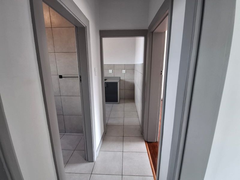 A clean, neutral hallway with tiled flooring providing access to a bathroom and a small kitchen area with built-in cabinetry.