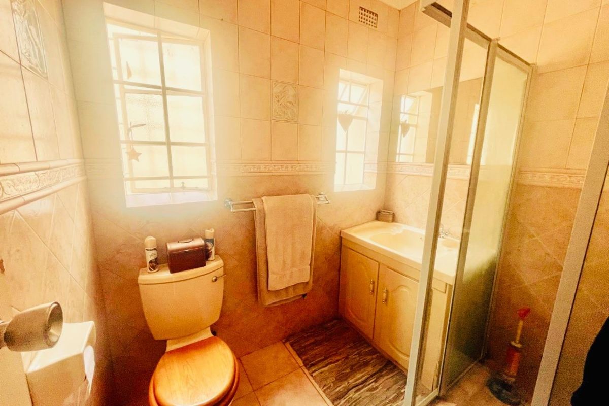 A functional bathroom featuring a built-in vanity, a toilet, and a glass-enclosed shower, finished with neutral wall tiles and natural light.