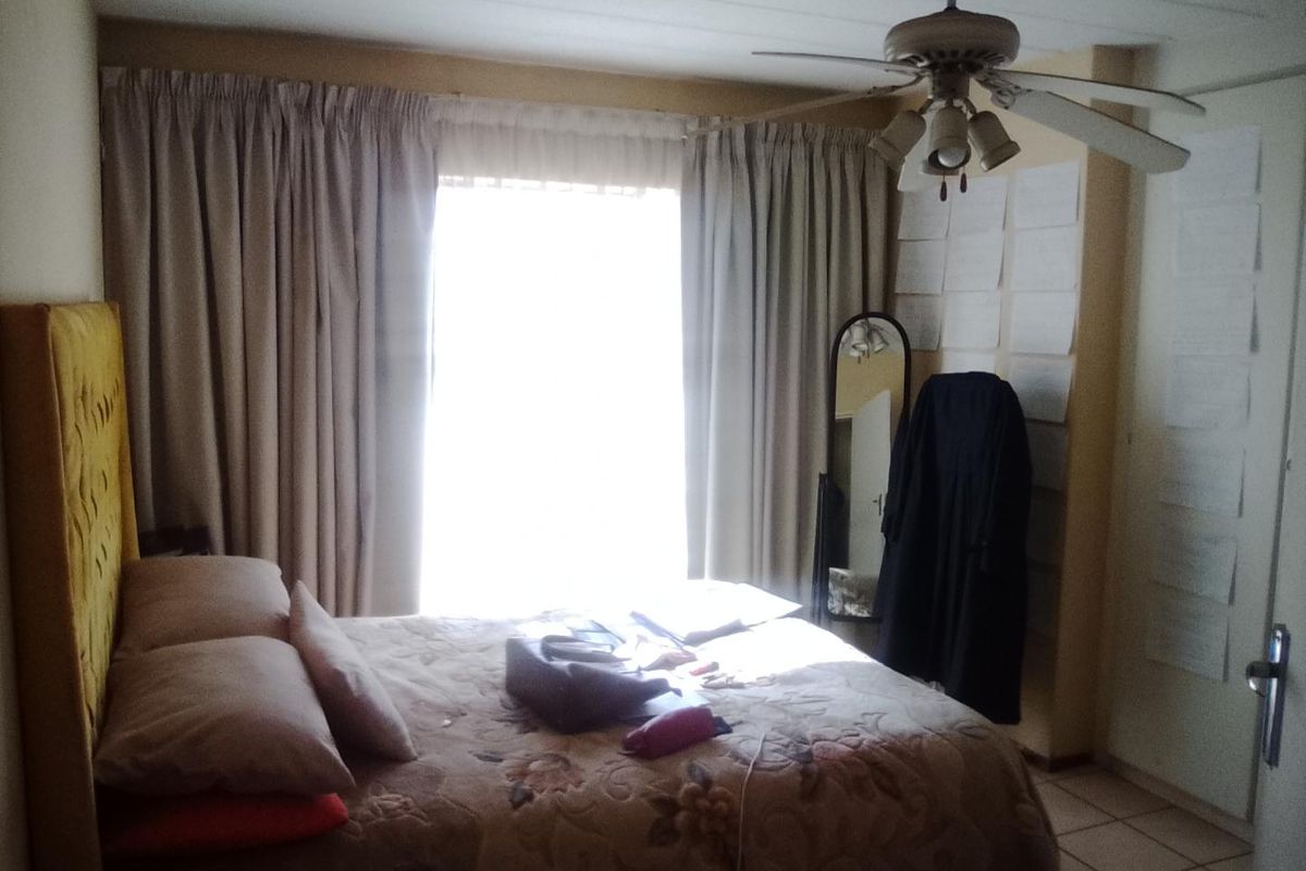 A bedroom featuring tiled flooring and a ceiling fan, with natural light entering through a large window.