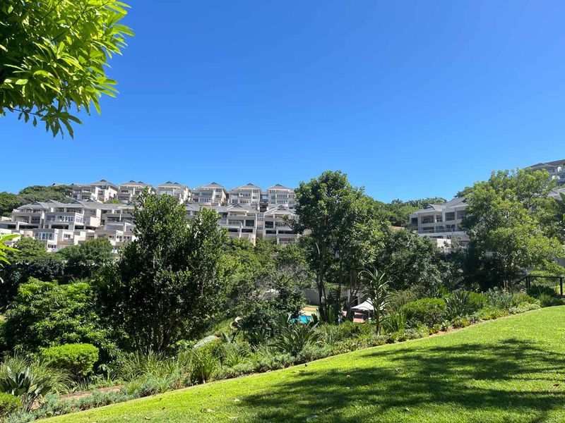 A scenic view of a multi-level apartment complex nestled within a lush, well-maintained landscaped garden setting.