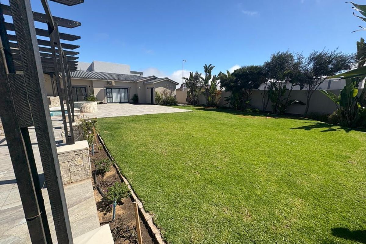 Spacious rear garden featuring a well-maintained lawn, paved patio area, and a timber pergola structure, providing an ideal space for outdoor living and entertaining.
