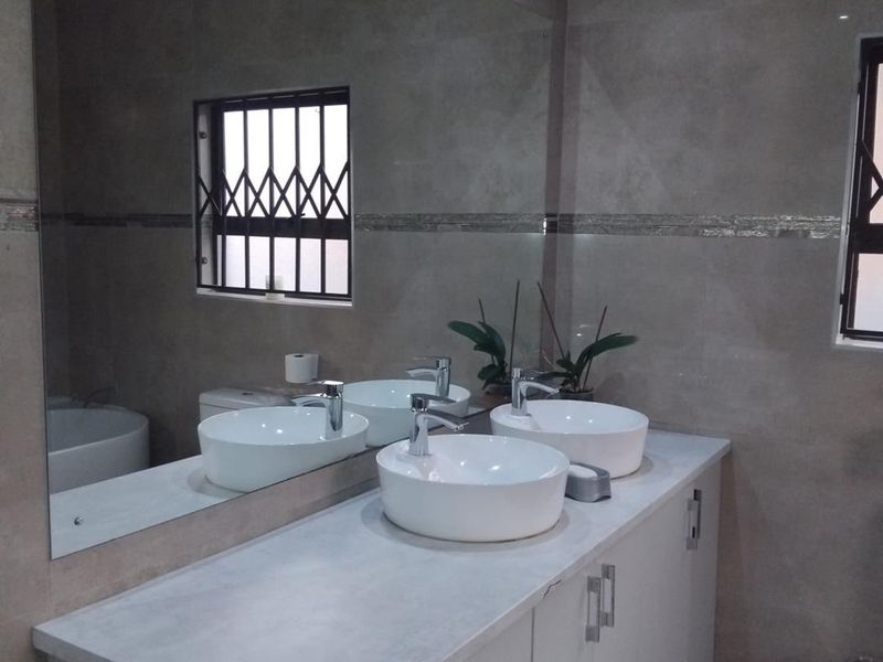 Modern bathroom featuring a double vanity with vessel sinks, chrome fixtures, and large wall-to-wall mirror, finished with contemporary neutral wall tiling.