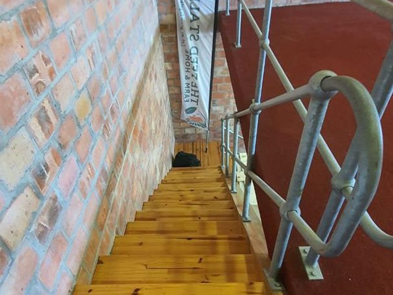A staircase featuring exposed brick walls, timber treads, and a sturdy metal handrail leading to a carpeted landing area.