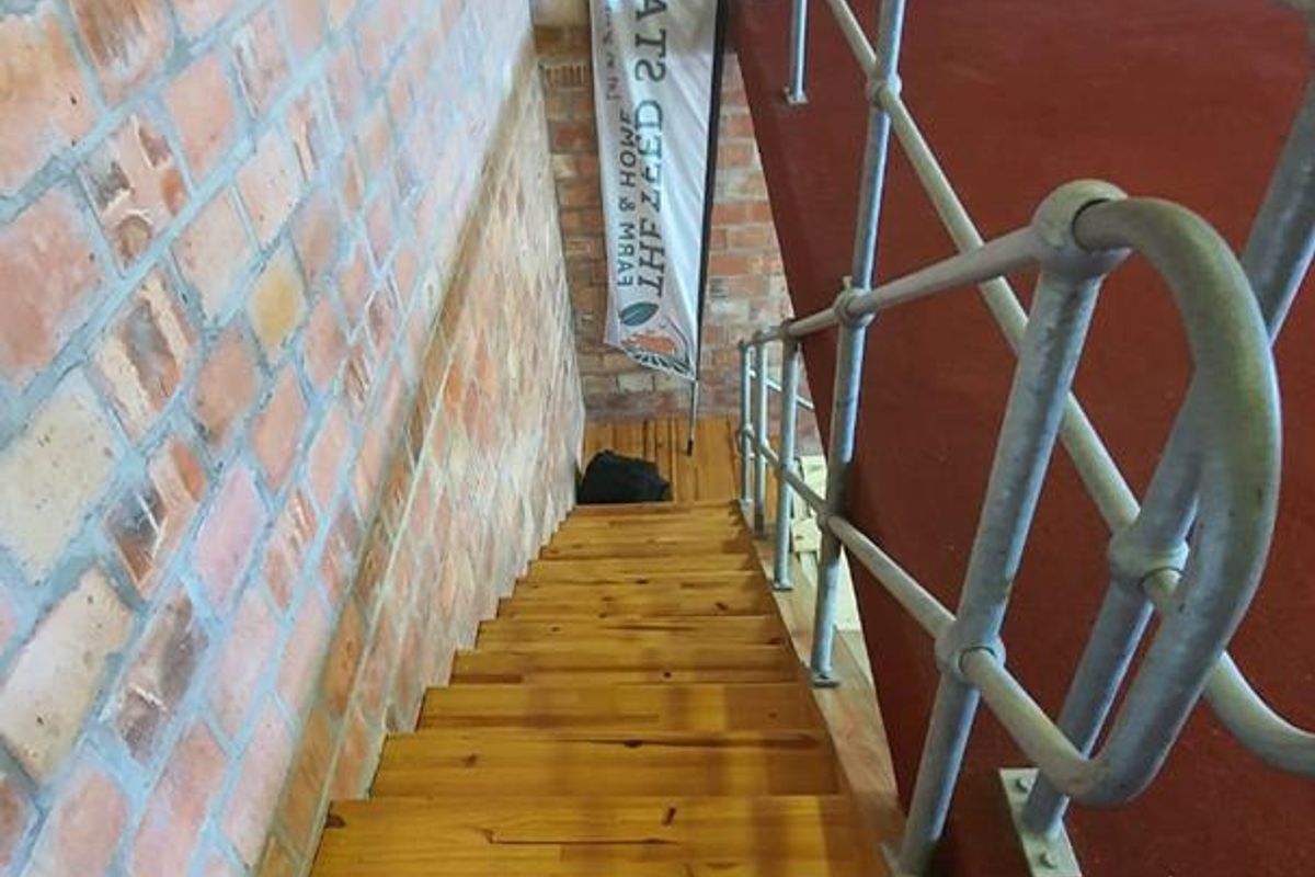 A staircase featuring exposed brick walls, timber treads, and a sturdy metal handrail leading to a carpeted landing area.