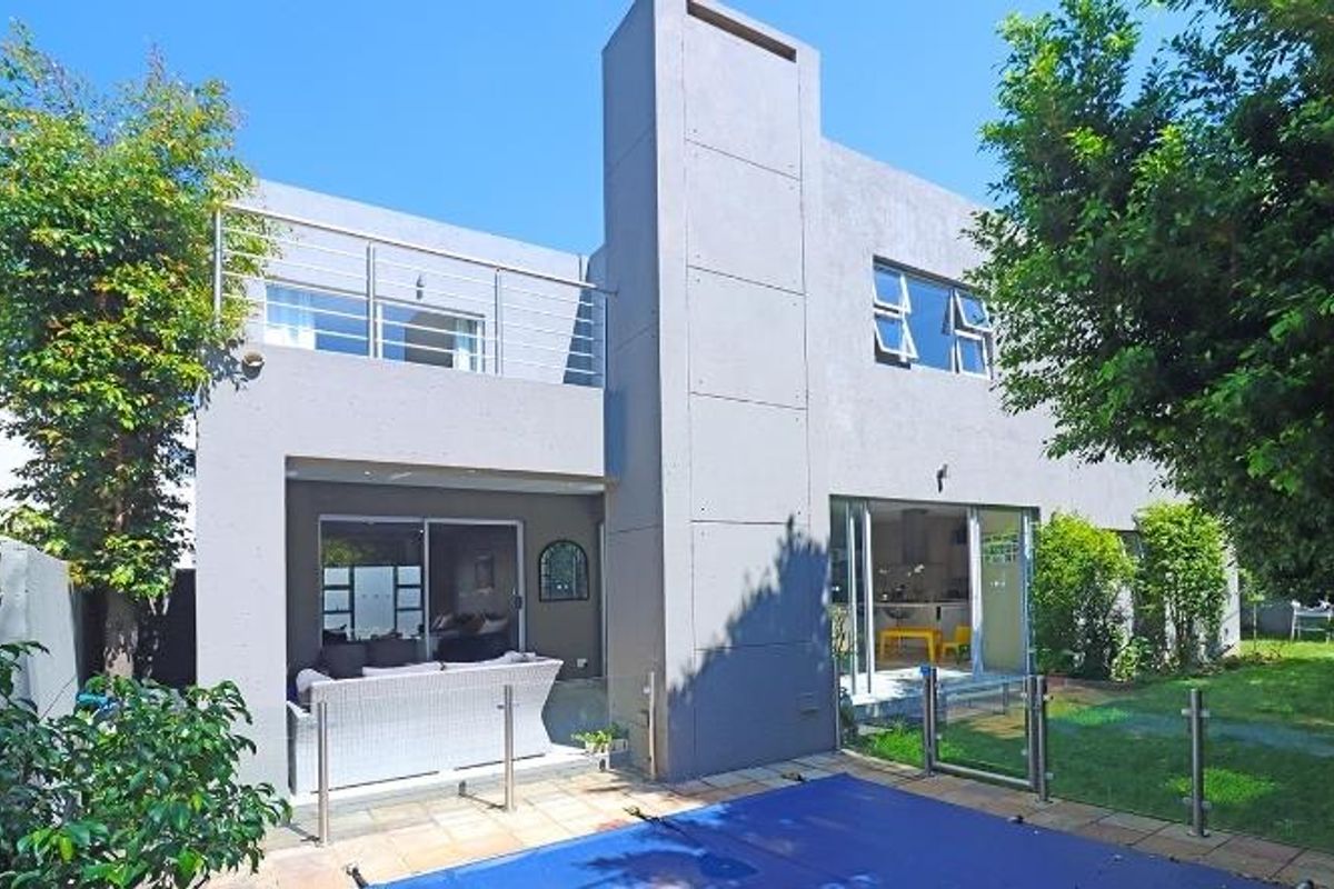 Rear view of a modern cluster home featuring a swimming pool, paved patio area, and an upper-level balcony with stainless steel railings.