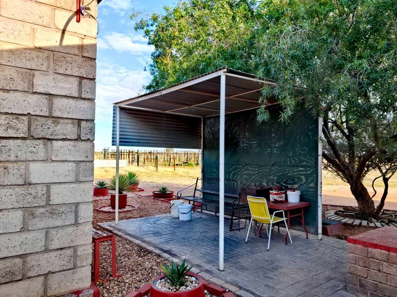 A covered outdoor patio area featuring paved flooring, metal roofing, and a privacy screen, providing a functional space for outdoor relaxation on the farm.