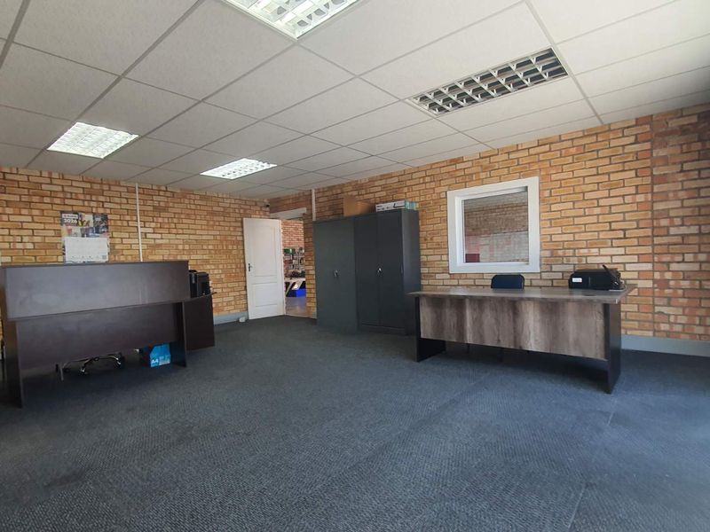 A functional office space featuring exposed brick walls, suspended ceilings with recessed lighting, and carpeted flooring, suitable for a professional business environment.