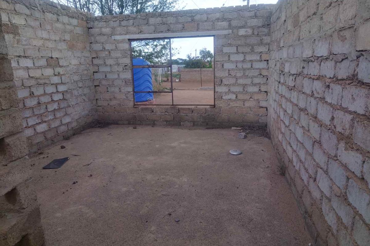 An unfinished room structure featuring exposed concrete block walls and a dirt floor, awaiting completion and interior finishes.