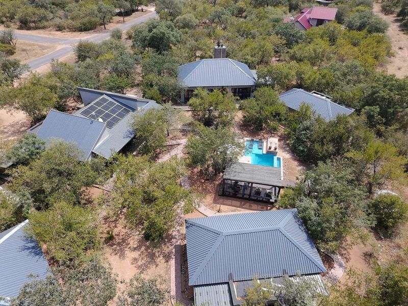 Aerial view of a guest house property featuring multiple buildings with metal roofs, solar panels, a swimming pool, and landscaped grounds.