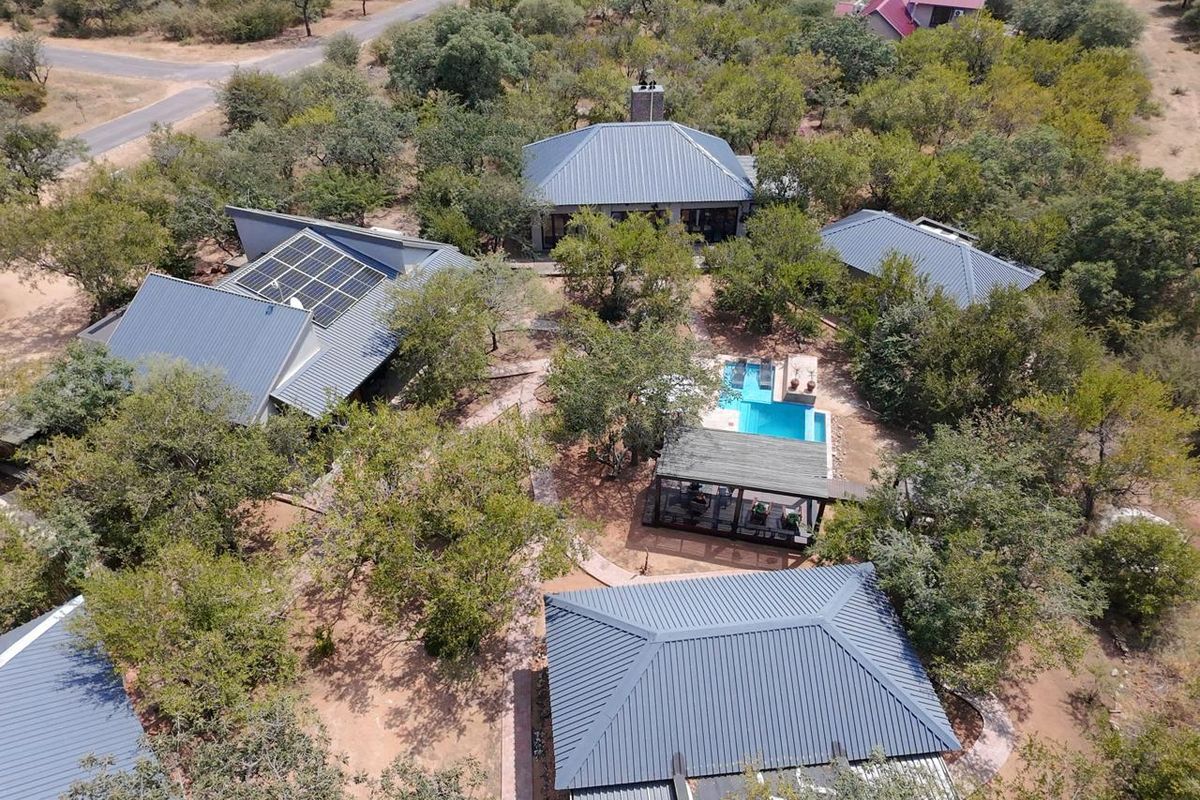 Aerial view of a guest house property featuring multiple buildings with metal roofs, solar panels, a swimming pool, and landscaped grounds.
