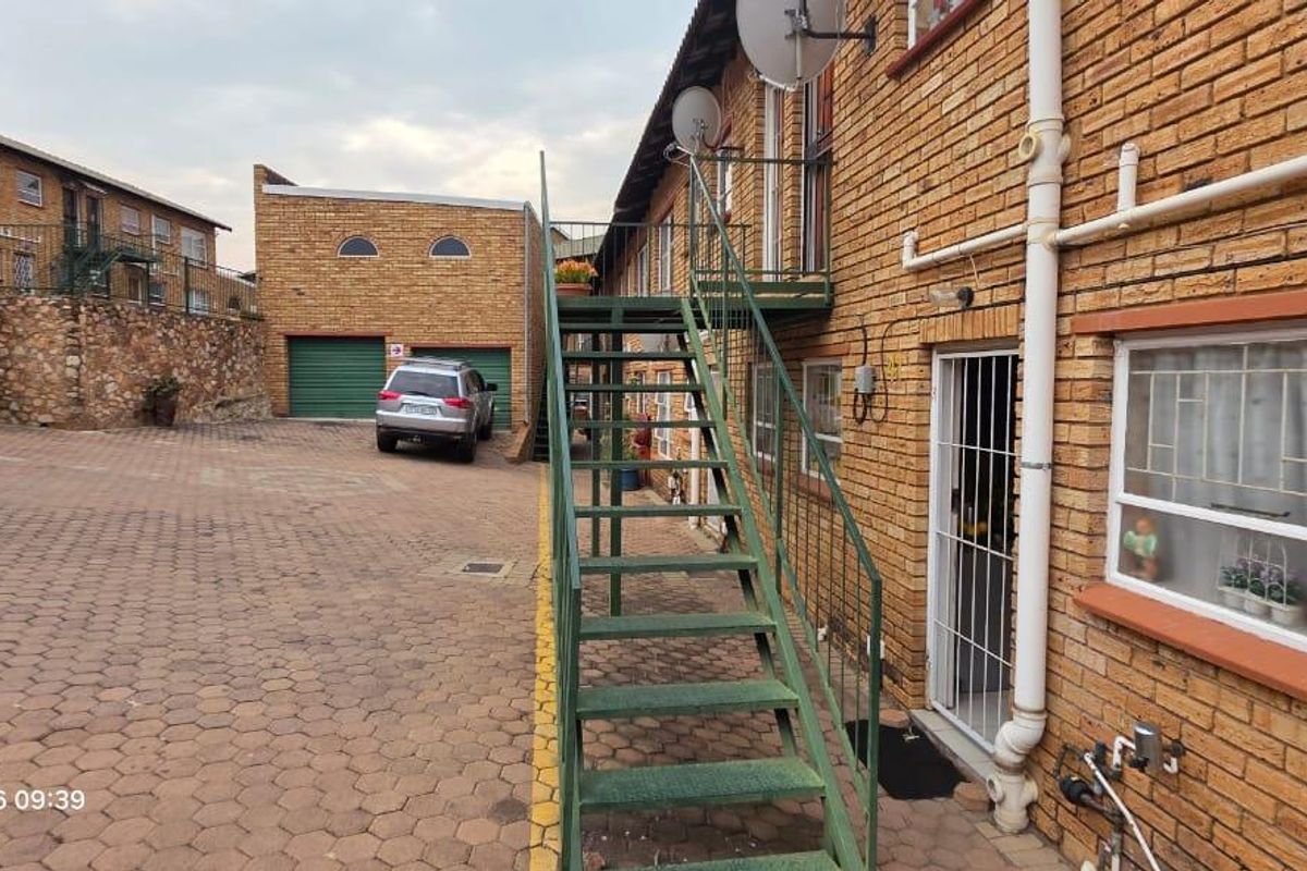 Exterior view of an apartment complex featuring a brick facade, paved parking area, and an external metal staircase providing access to upper levels.
