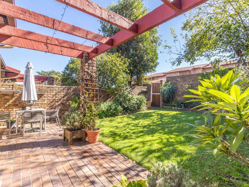 A private rear garden featuring a paved patio area with a timber pergola, established lawn, and brick boundary walls.