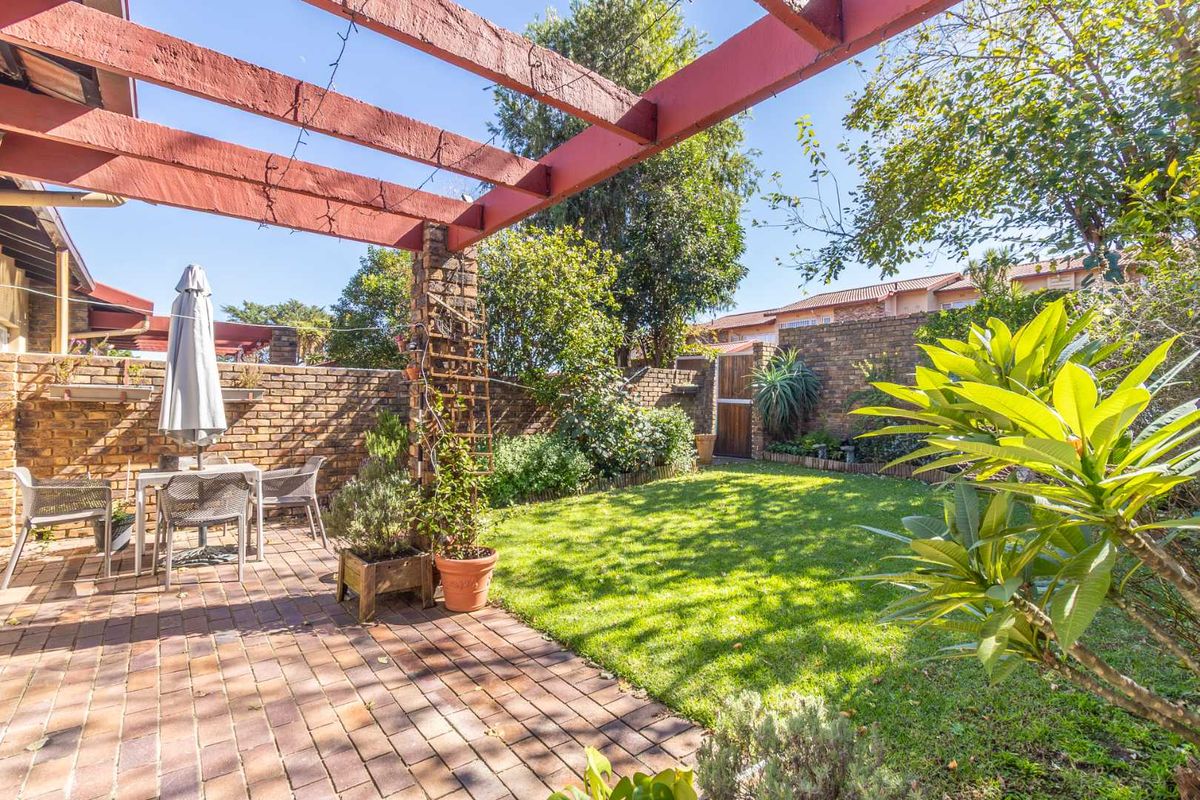 A private rear garden featuring a paved patio area with a timber pergola, established lawn, and brick boundary walls.