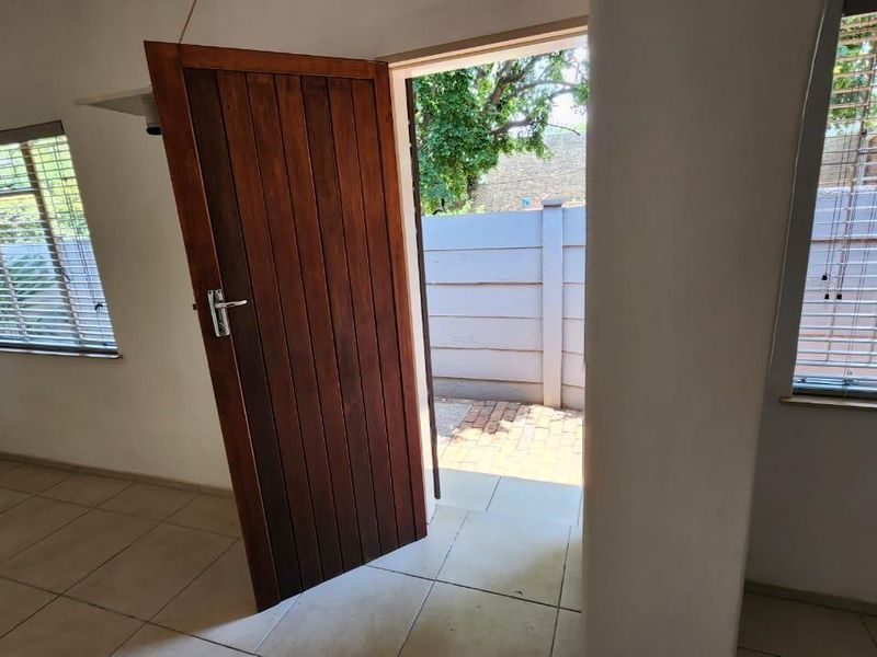 An empty living area featuring tiled flooring, timber door access to a paved outdoor space, and venetian blinds on the windows.