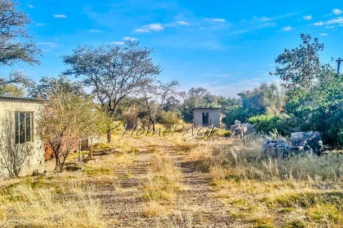 An exterior view of the small holding grounds featuring dry, unmaintained vegetation, a basic structure, and scattered building materials on the property.