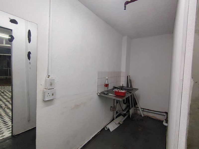 A small utility or scullery area featuring a stainless steel sink, tiled splashback, and exposed plumbing, requiring cosmetic updates and maintenance.