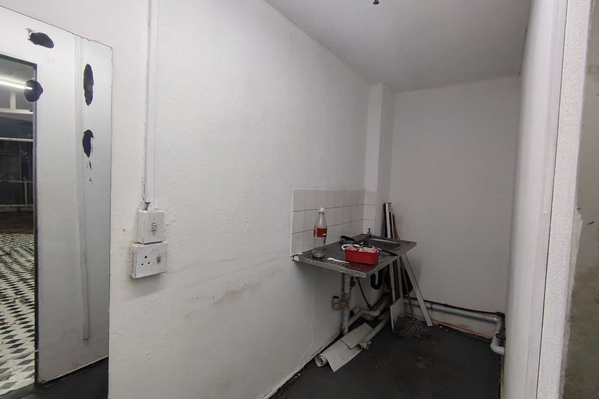 A small utility or scullery area featuring a stainless steel sink, tiled splashback, and exposed plumbing, requiring cosmetic updates and maintenance.