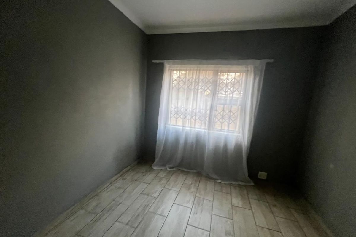 An empty bedroom featuring dark grey walls, light wood-look tiled flooring, and a window fitted with a security gate.