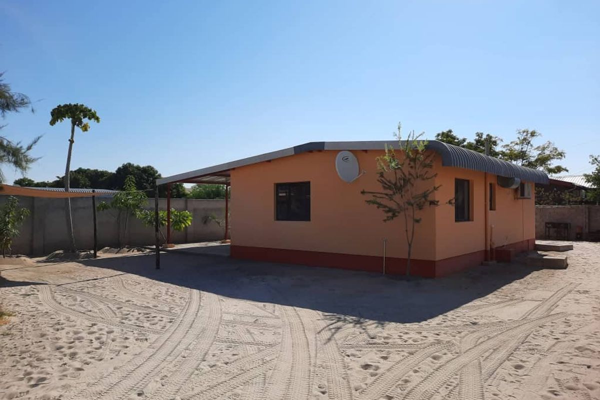 Exterior view of a single-story house featuring a covered patio area, metal roof, and sandy yard surroundings.